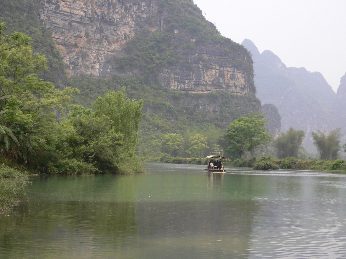 A bamboo raft beneath karst cliffs at Mingshi · Chongzuo